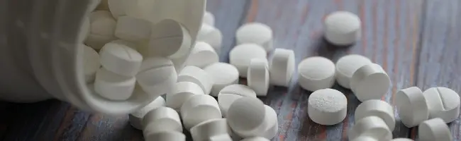 Close-up of white pills spilling out of a bottle onto a wooden surface, symbolizing medication or pharmaceutical products.